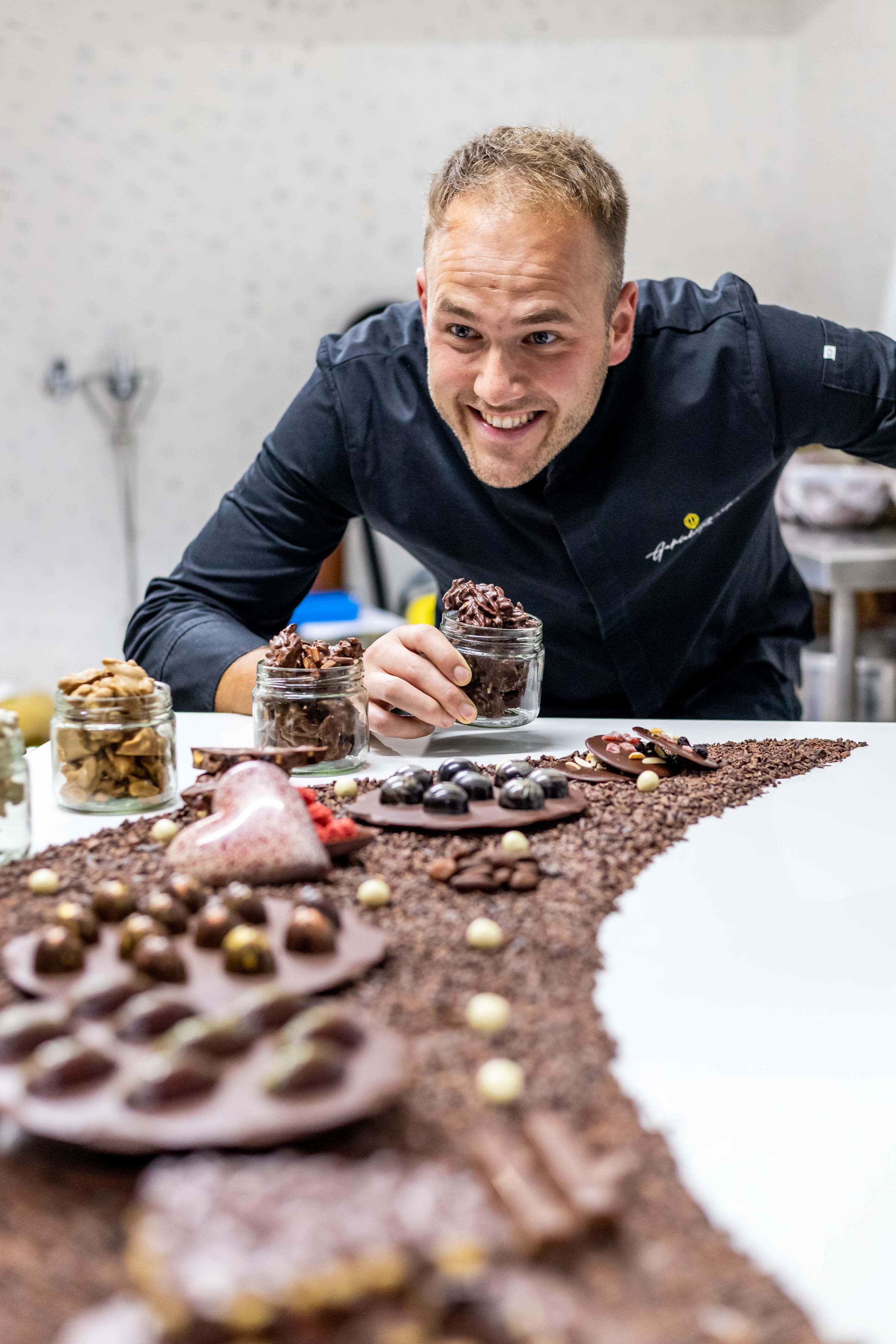Chocolatier holding cocoa nibs with chocolate pieces and beans arranged artistically