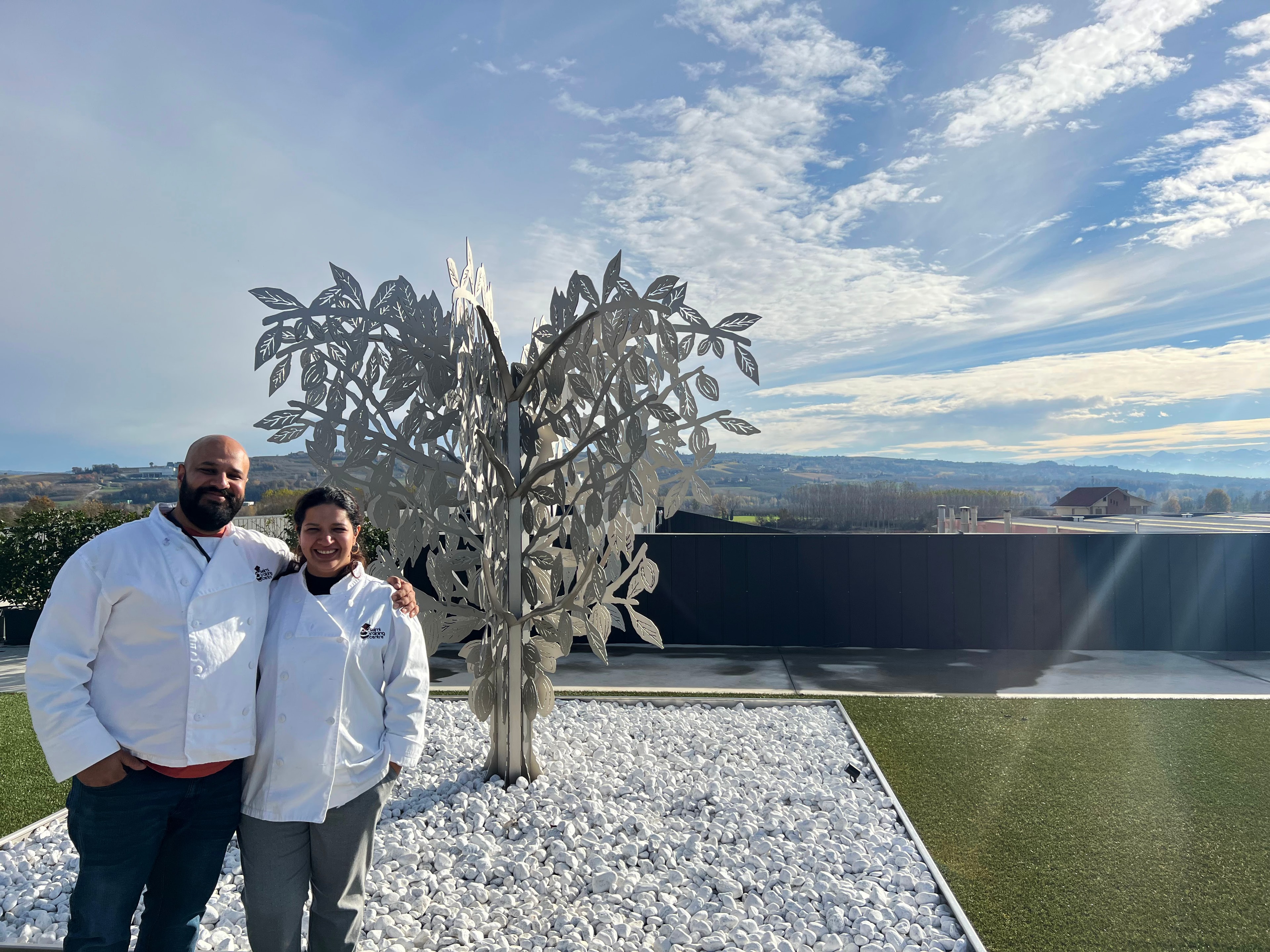 Priyanka and Amritanshu in white chef coats with modern tree sculpture in background